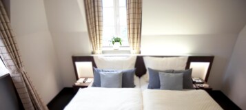 Habitación de hotel con una cama grande, dos mesitas de noche y una ventana con cortinas.