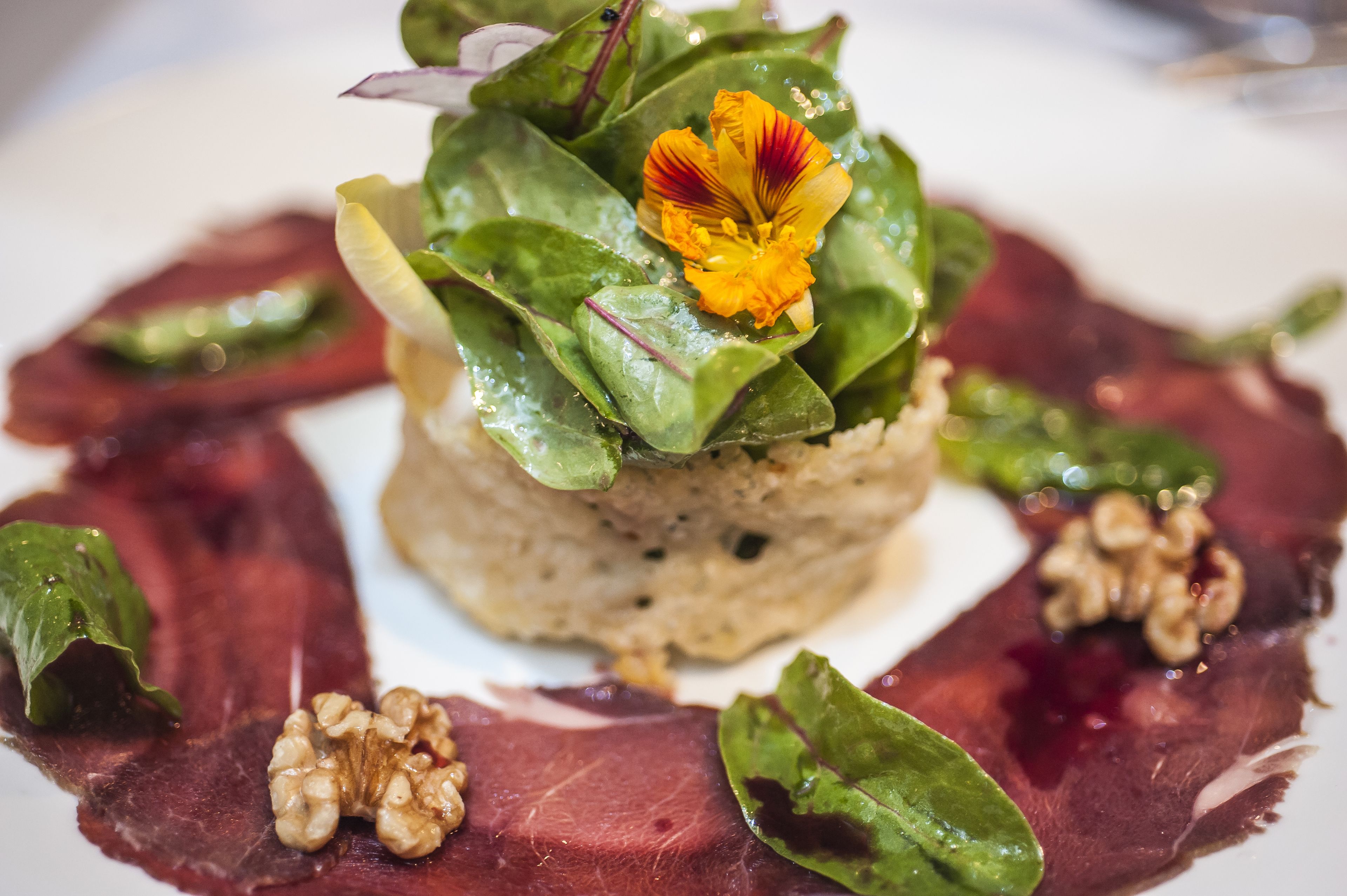Une assiette contenant un plat composé de plusieurs couches, des légumes verts à feuilles, une fleur et des noix.