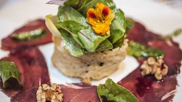 Une assiette contenant un plat composé de plusieurs couches, des légumes verts à feuilles, une fleur et des noix.