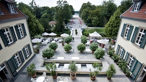A courtyard with outdoor seating, potted plants, and a view of a lake. - Schloss Berge (Gelsenkirchen)