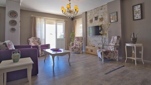 Un salon agrémenté d’un lustre, de fauteuils à motifs floraux, d’une table blanche et d’un mur en pierre avec une cheminée.
