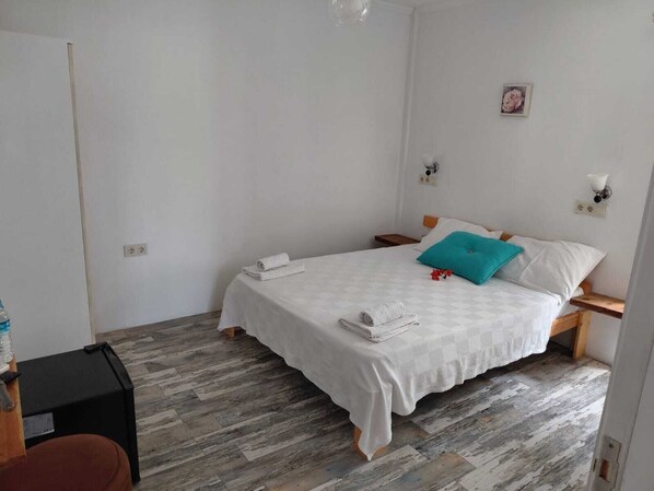 Una habitación pequeña y limpia con una cama, una mesita de noche y piso de madera.