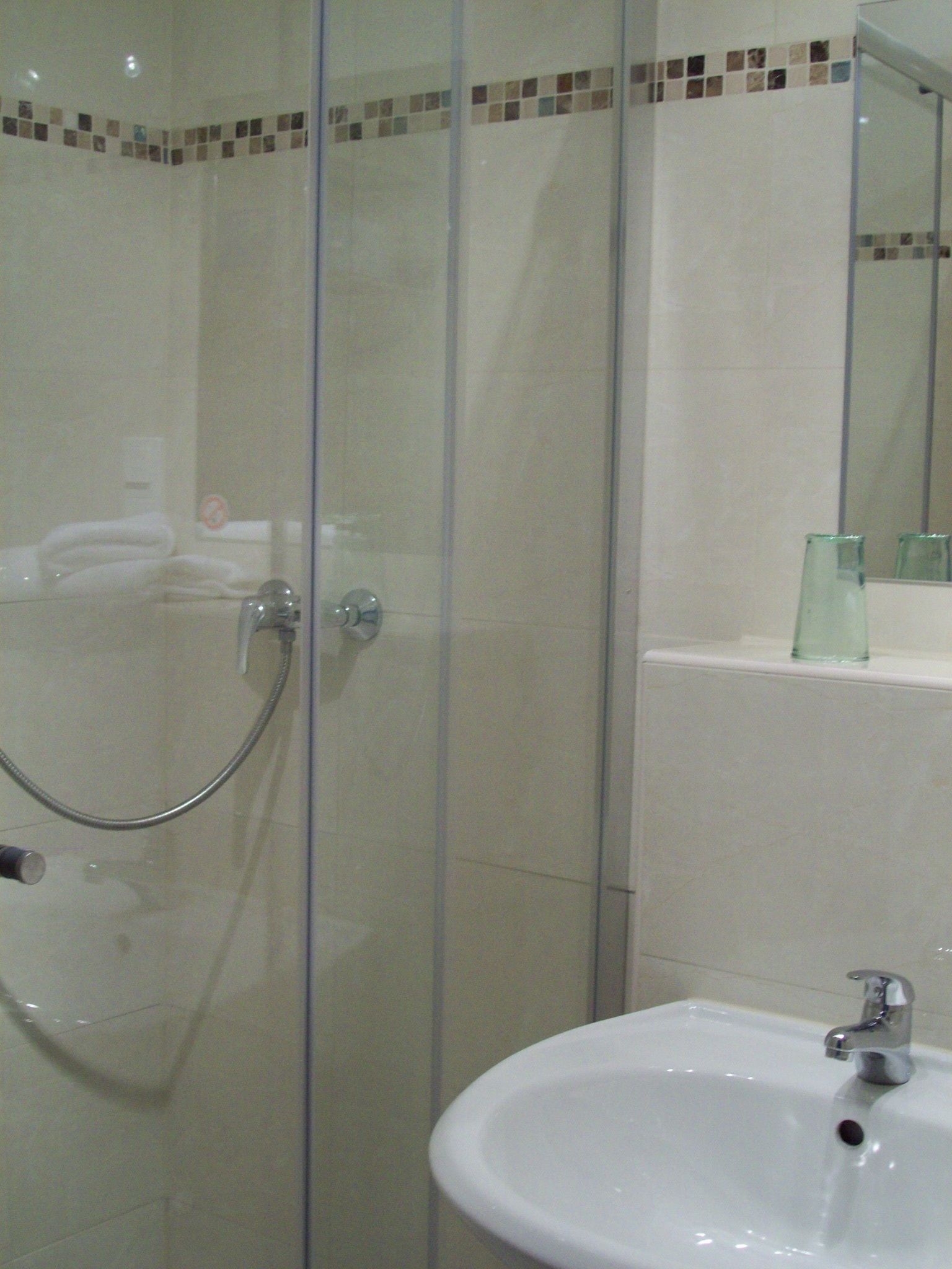 Een badkamer met een douchecabine van glas, een witte wastafel en een spiegel erboven.