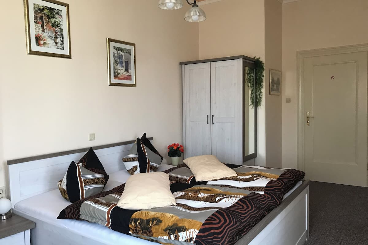 A neatly arranged bedroom with a bed, a wardrobe, and two framed pictures on the wall.