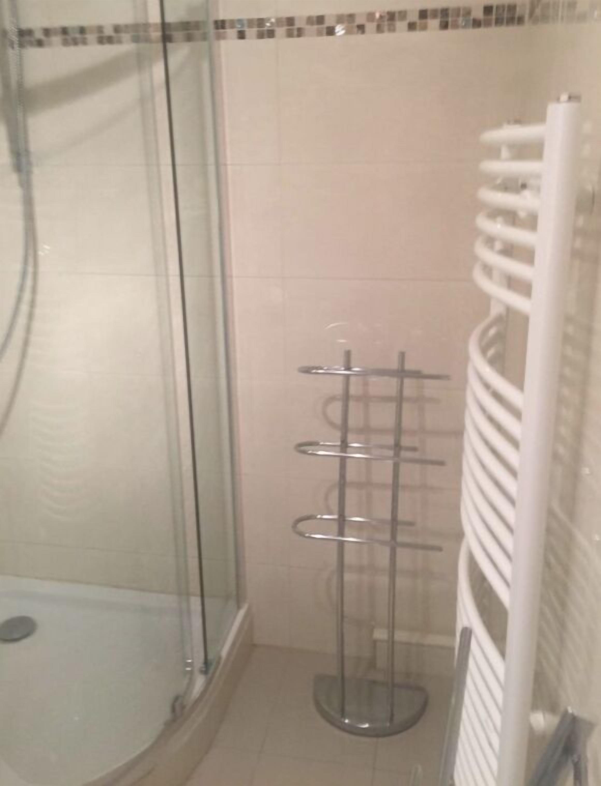 A bathroom with a glass shower enclosure, a white towel rack, and a tiled wall.