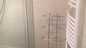 A bathroom with a glass shower enclosure, a white towel rack, and a tiled wall.