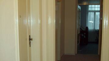 A hallway with a carpeted floor, a door on the left, and a window with a light fixture in the background.