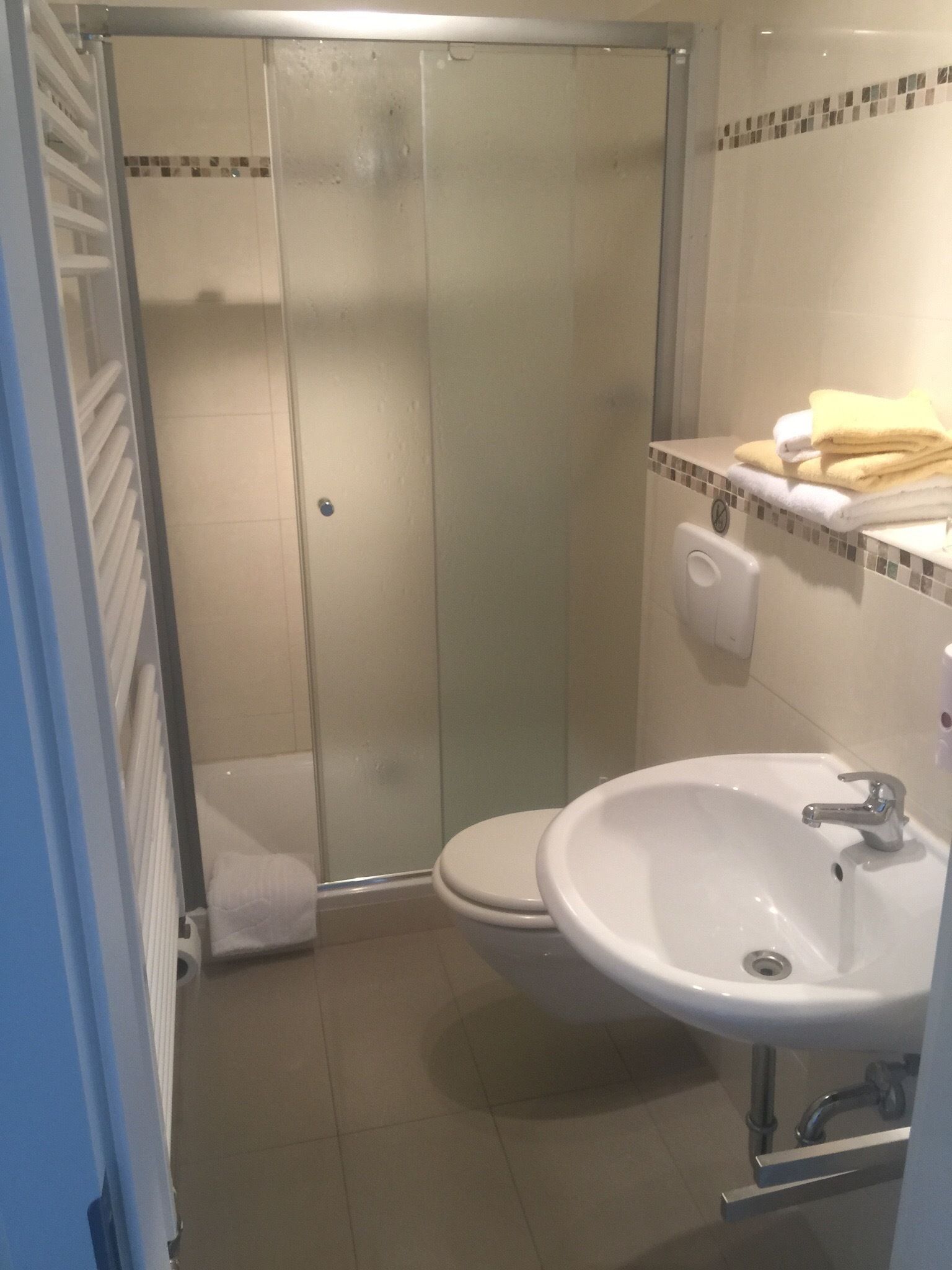 Une salle de bain avec une douche à parois de verre, un lavabo blanc et un porte-serviettes.