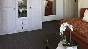 A hotel room with a large wardrobe, a bed with a patterned bedspread, a glass coffee table with a vase of flowers, and a mirror on the wall. - Pension Villa Else (Heidenau)