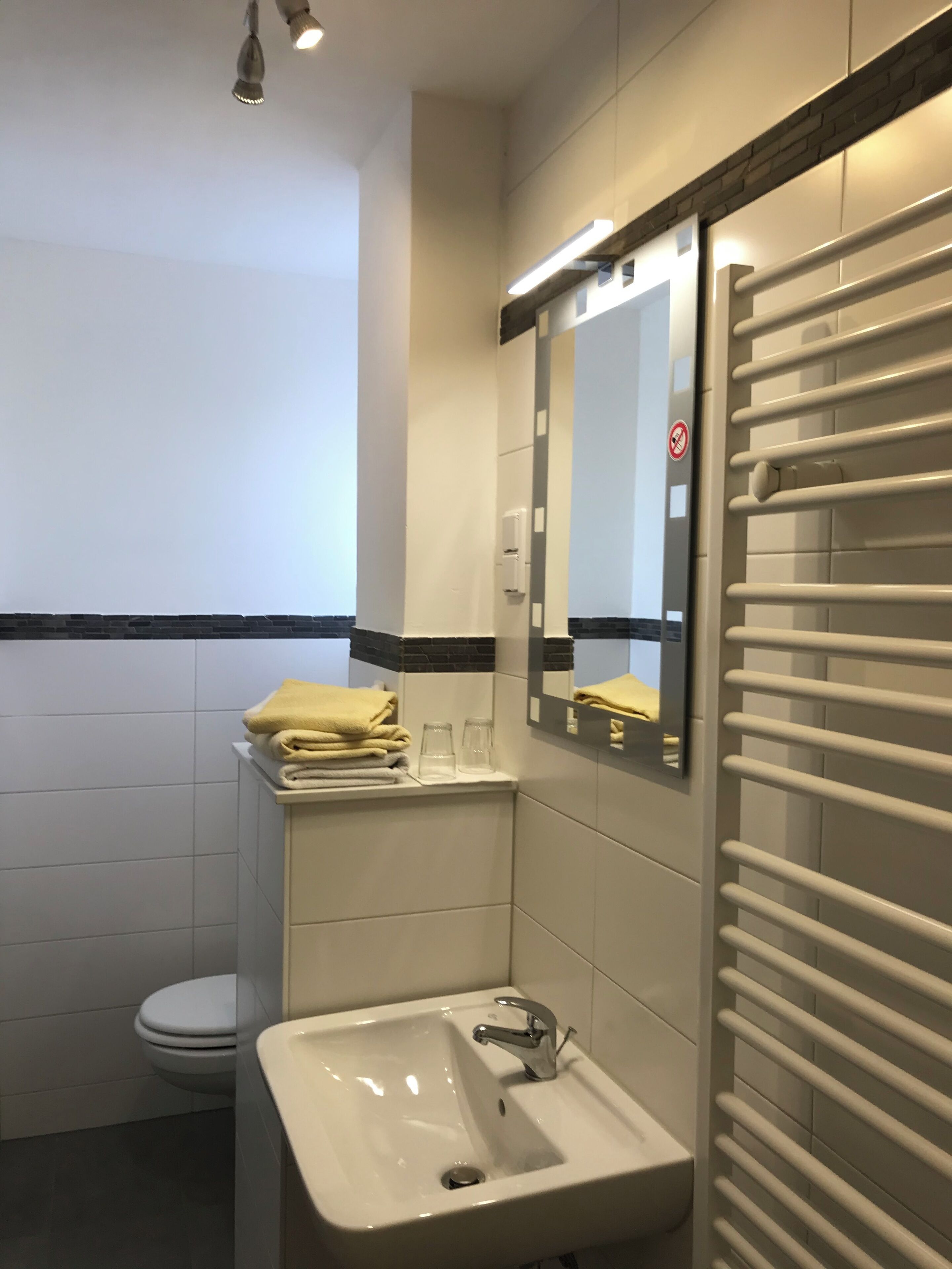 Un baño con lavamanos blanco, espejo, toallero y retrete.