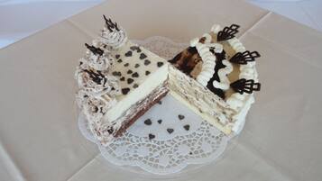 Un pastel con glaseado blanco y decoraciones de chocolate sobre un plato de vidrio transparente con un copo de encaje debajo.