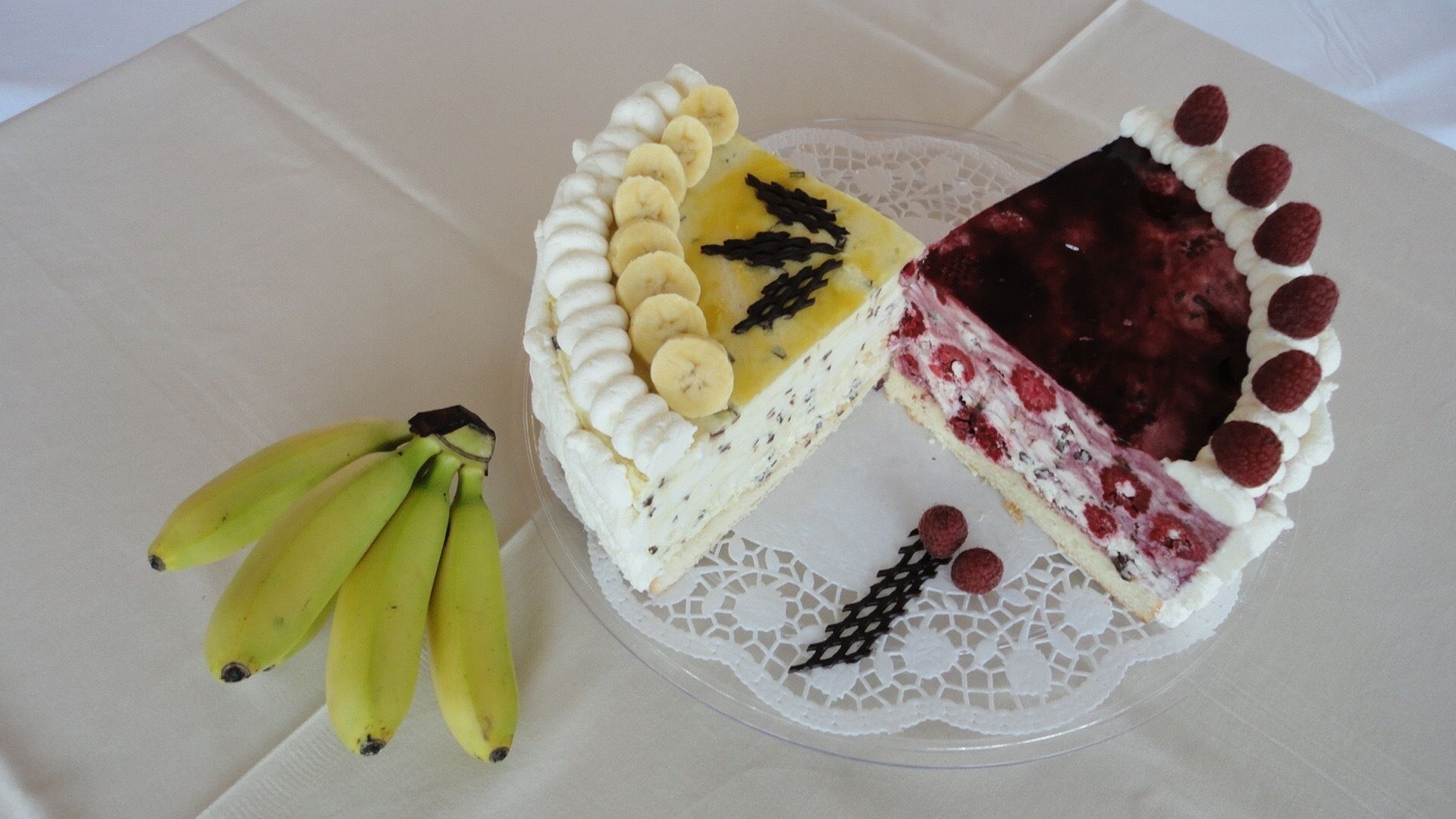 A cake with a slice missing, decorated with bananas and chocolate shavings, and a side of bananas.