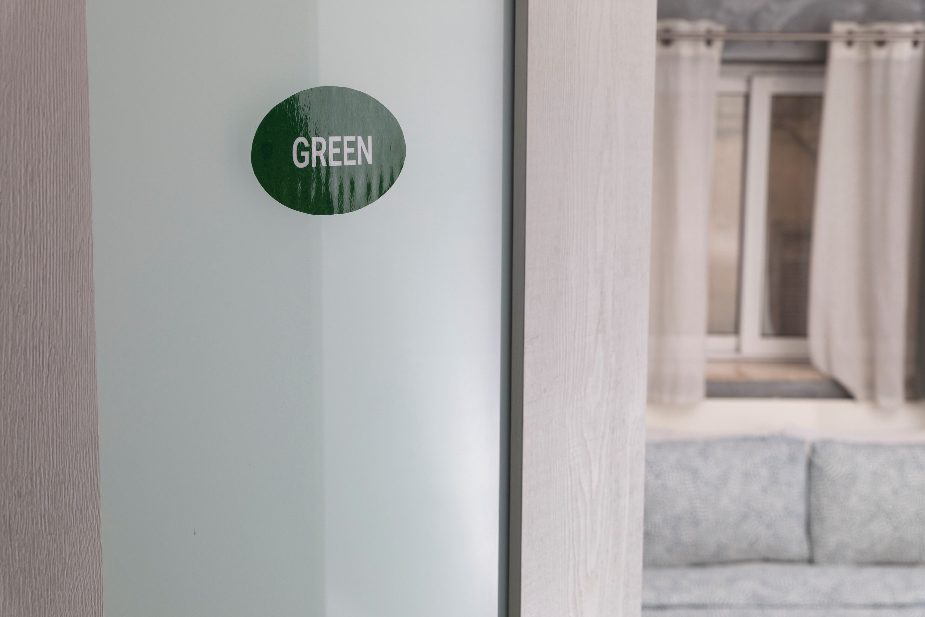 Un panneau vert sur un mur, avec un arrière-plan flou d’une pièce comprenant un canapé gris et des rideaux.