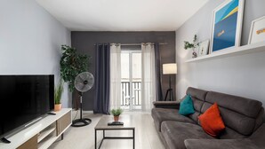 A modern living room with a flat-screen TV, a sofa with colorful cushions, a coffee table, a potted plant, and a standing fan. - Modern 3 Bedroom 3 Bathroom Near Balluta Bay Sliema (St. Julian's)