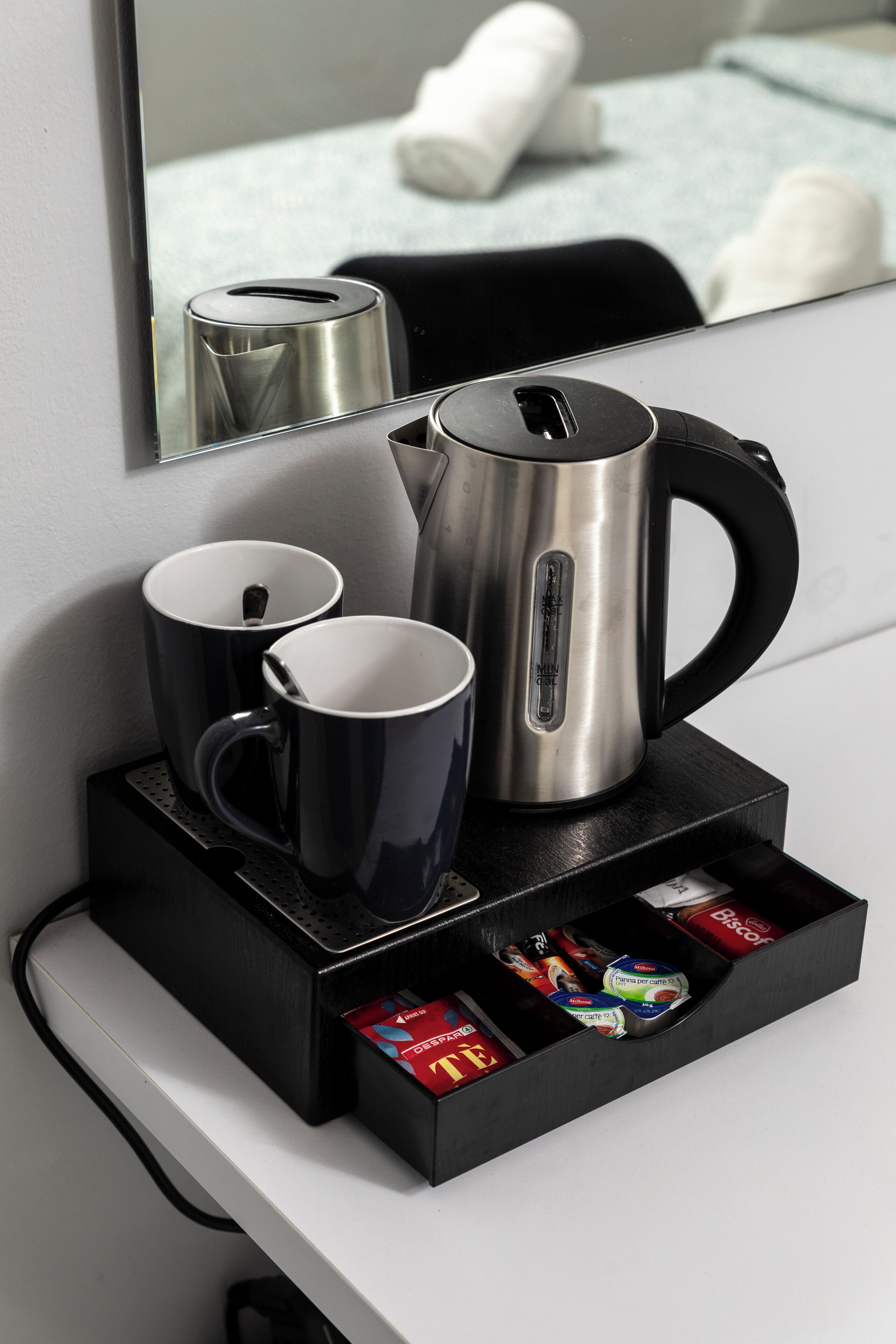 Una estación de café con una tetera, dos tazas y una bandeja con aperitivos.