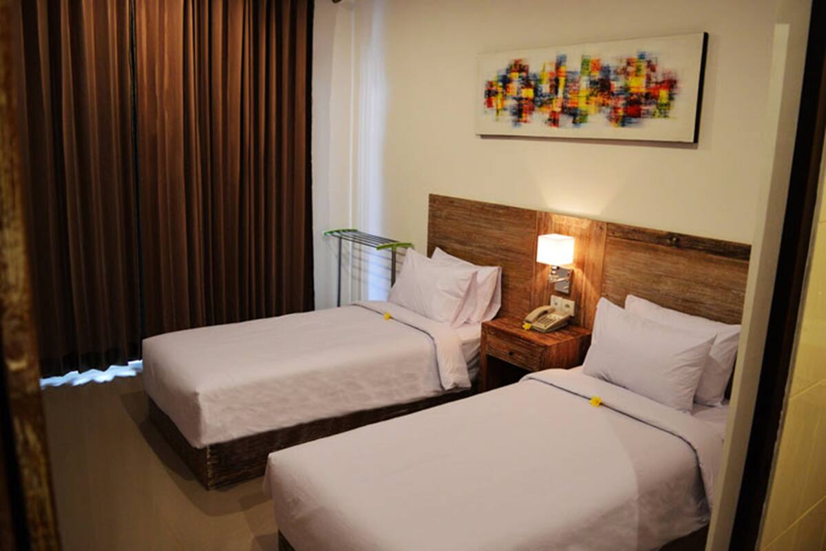 A hotel room with two beds, a wooden headboard, a nightstand with a lamp, and a colorful abstract painting on the wall.