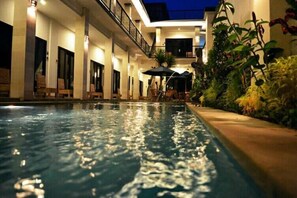 A swimming pool with lounge chairs and umbrellas, surrounded by plants and a building with a balcony. - Tirtha Canggu Suites (Tibubeneng)