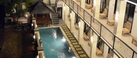 Un hotel con piscina, zona de estar al aire libre y un espacio cubierto con escaleras que conducen a los pisos superiores.