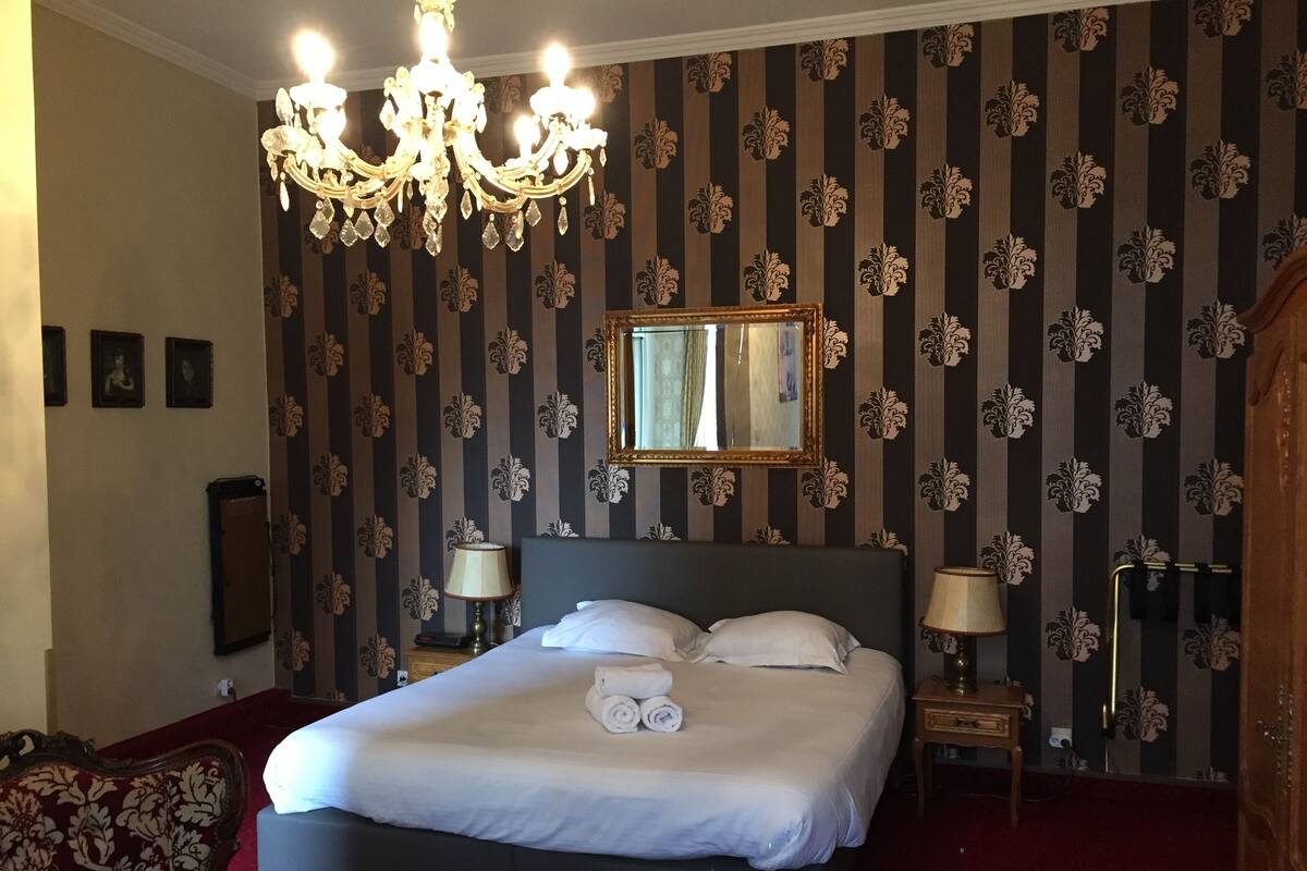 Hotellihuone, jossa on suuri sänky, kaksi yöpöytää, kattokruunu, peili ja raidallinen tapetti.