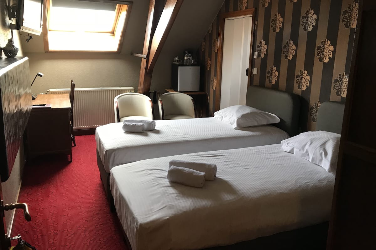 Hotellihuone, jossa on kaksi sänkyä, työpöytä, tuoli, patteri ja televisio.