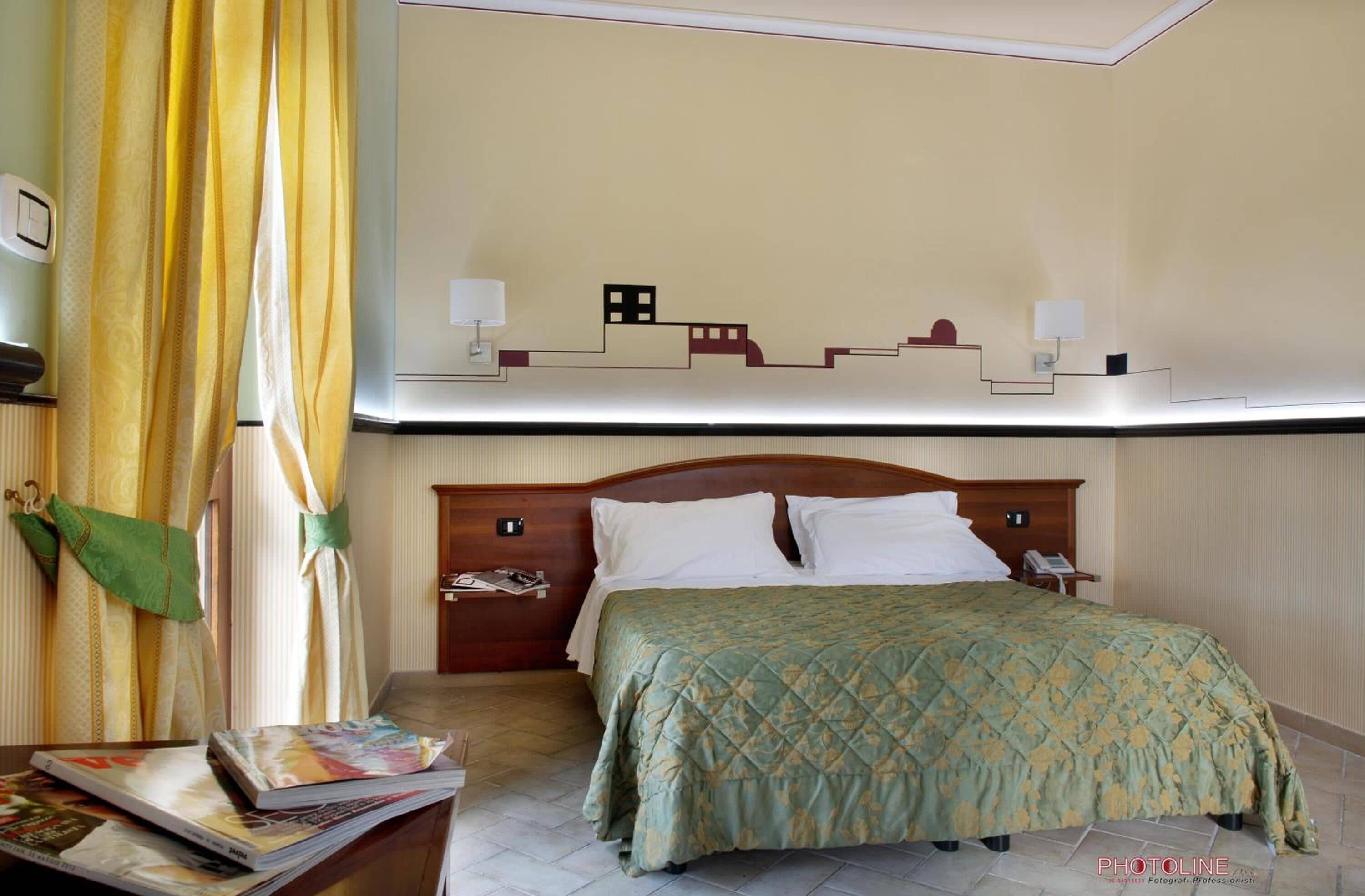A hotel room with a bed, bedside table, lamp, and a wall-mounted artwork.