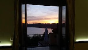 A room with a large window overlooking a body of water during sunset. - Villa Degli Angeli (Castel Gandolfo)