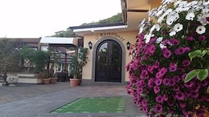 A building with a black door and a sign above it. There are potted plants and a green mat in front of the door. - Villa Degli Angeli (Castel Gandolfo)