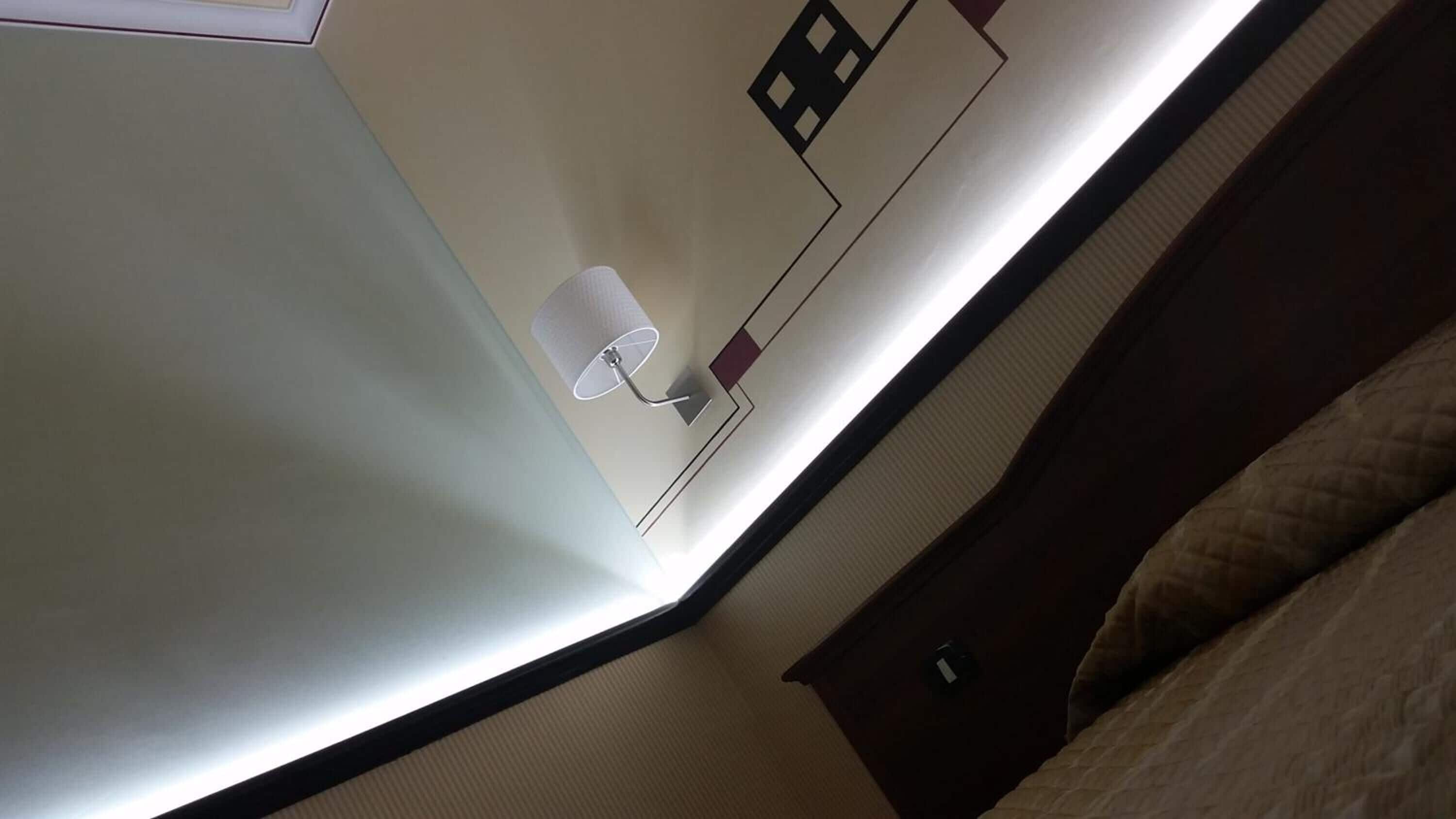 Un coin de pièce avec un lit, une lampe fixée au mur et une prise de courant.