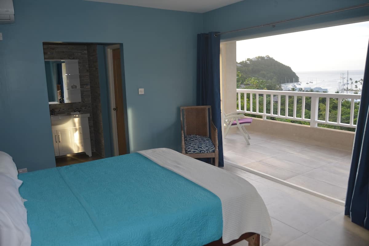 A bedroom with a balcony, a kitchenette, and a view of the sea.