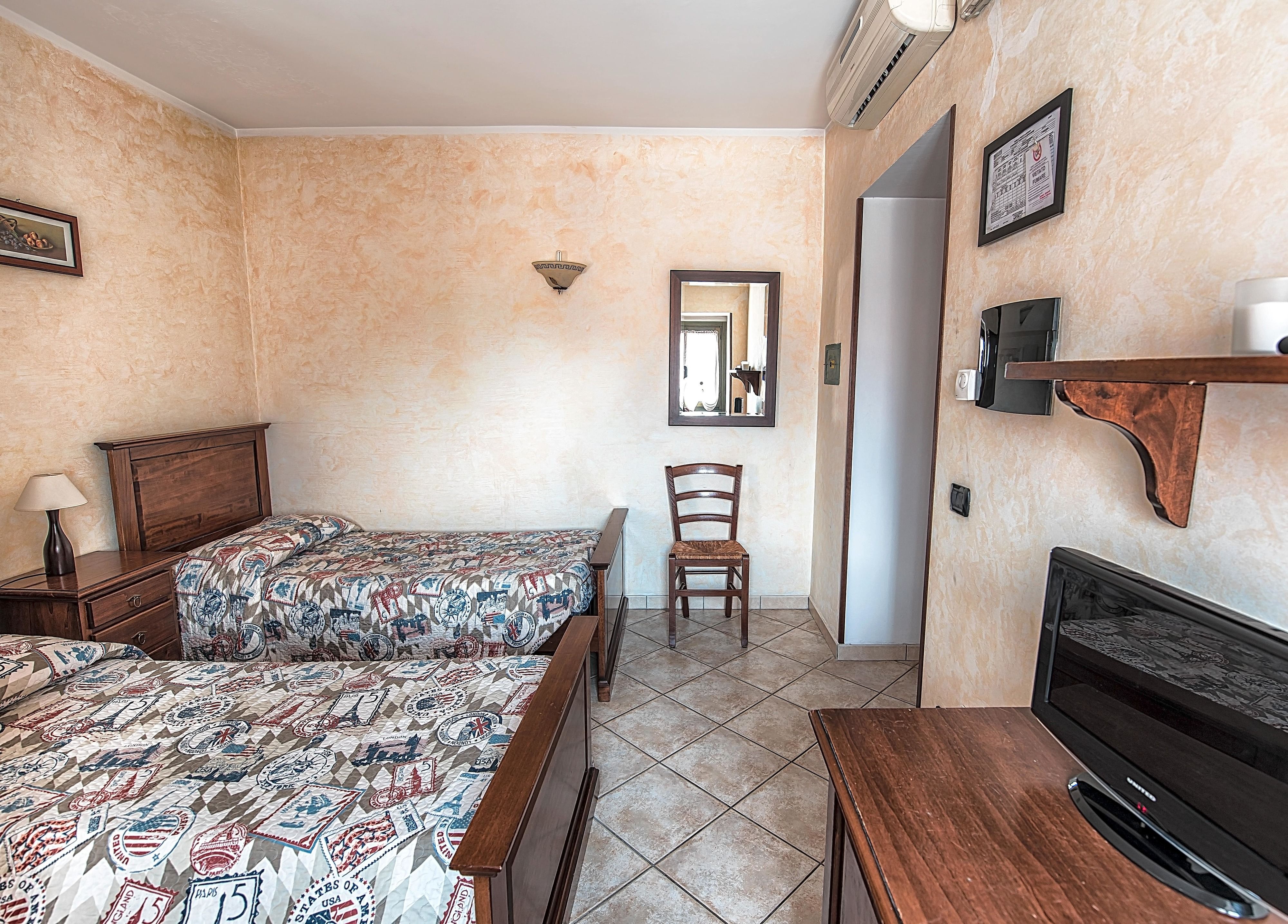 Habitación de hotel con dos camas, una silla, un televisor y una estantería con espejo e imagen.