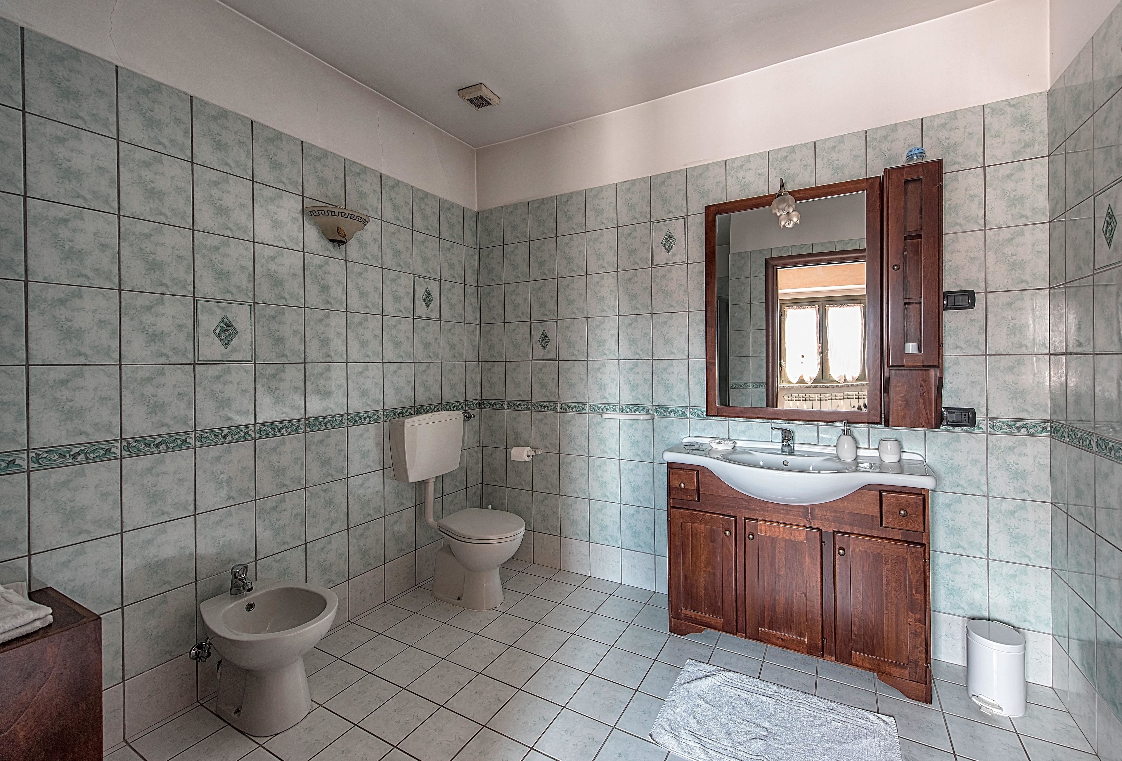 A bathroom with a toilet, bidet, sink, and wooden cabinet.