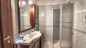 Un baño con tocador de madera, lavamanos, espejo y cabina de ducha con paredes de vidrio.