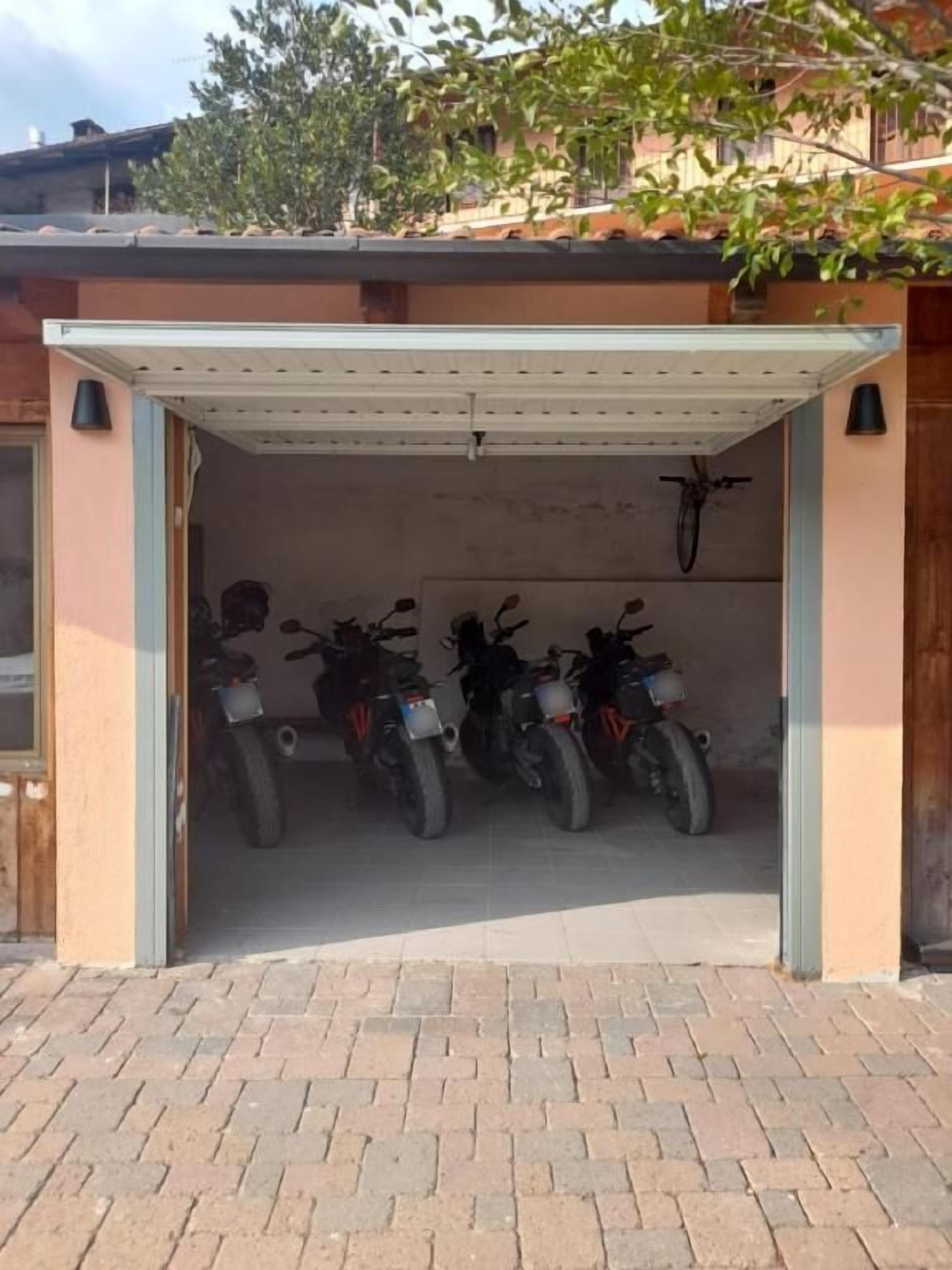 A covered motorcycle parking area with a brick floor and a building in the background.