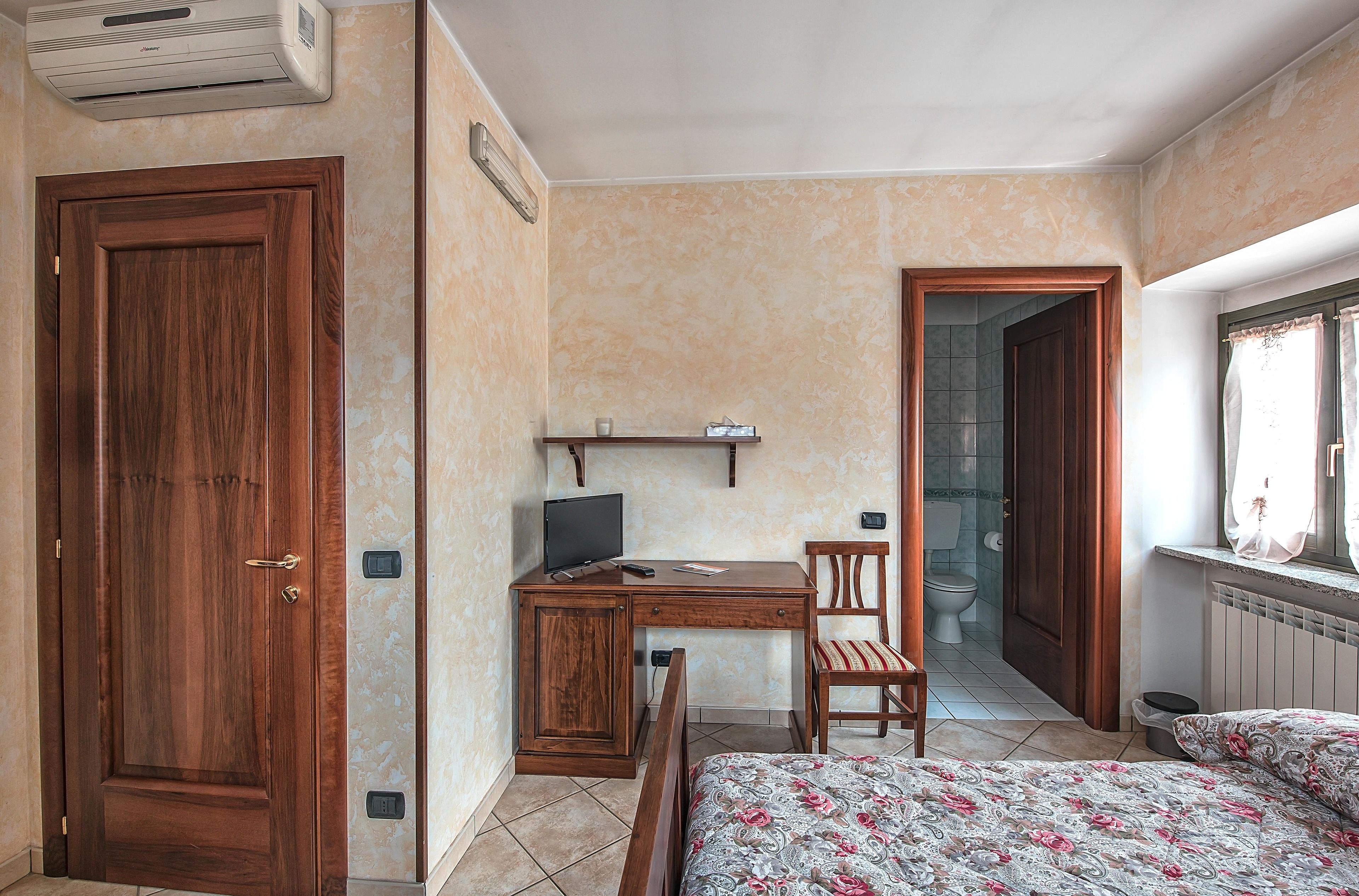 Un dormitorio con puerta de madera, un escritorio con computadora, una silla, una cama con ropa de cama estampada y una ventana con cortinas.