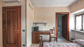 Un dormitorio con puerta de madera, un escritorio con computadora, una silla, una cama con ropa de cama estampada y una ventana con cortinas.
