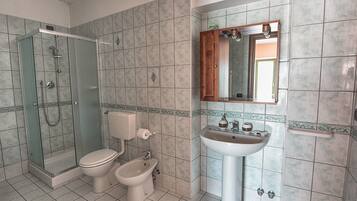 A bathroom with a glass-enclosed shower, a toilet, a bidet, and a sink with a mirror above it.