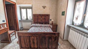 A bedroom with a wooden bed, a nightstand, a chair, a window with curtains, and a radiator.
