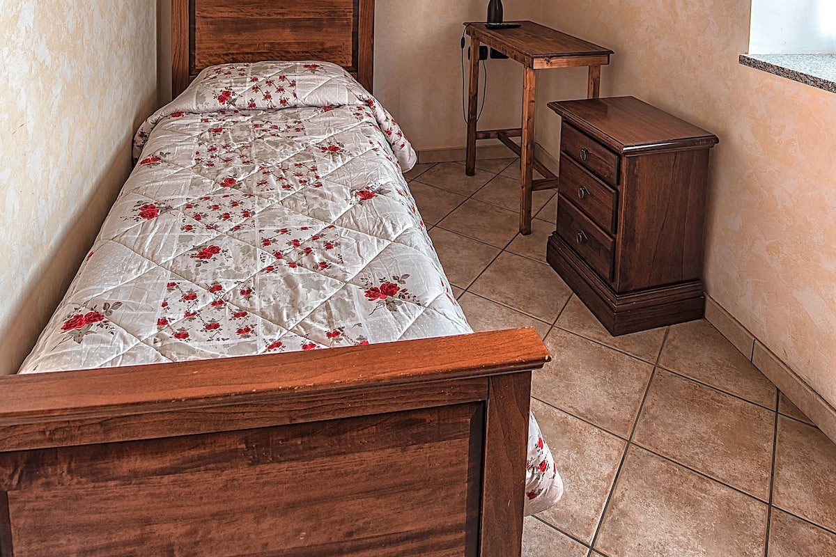 A bedroom with a wooden bed, a small wooden nightstand, a night lamp, and a picture on the wall.