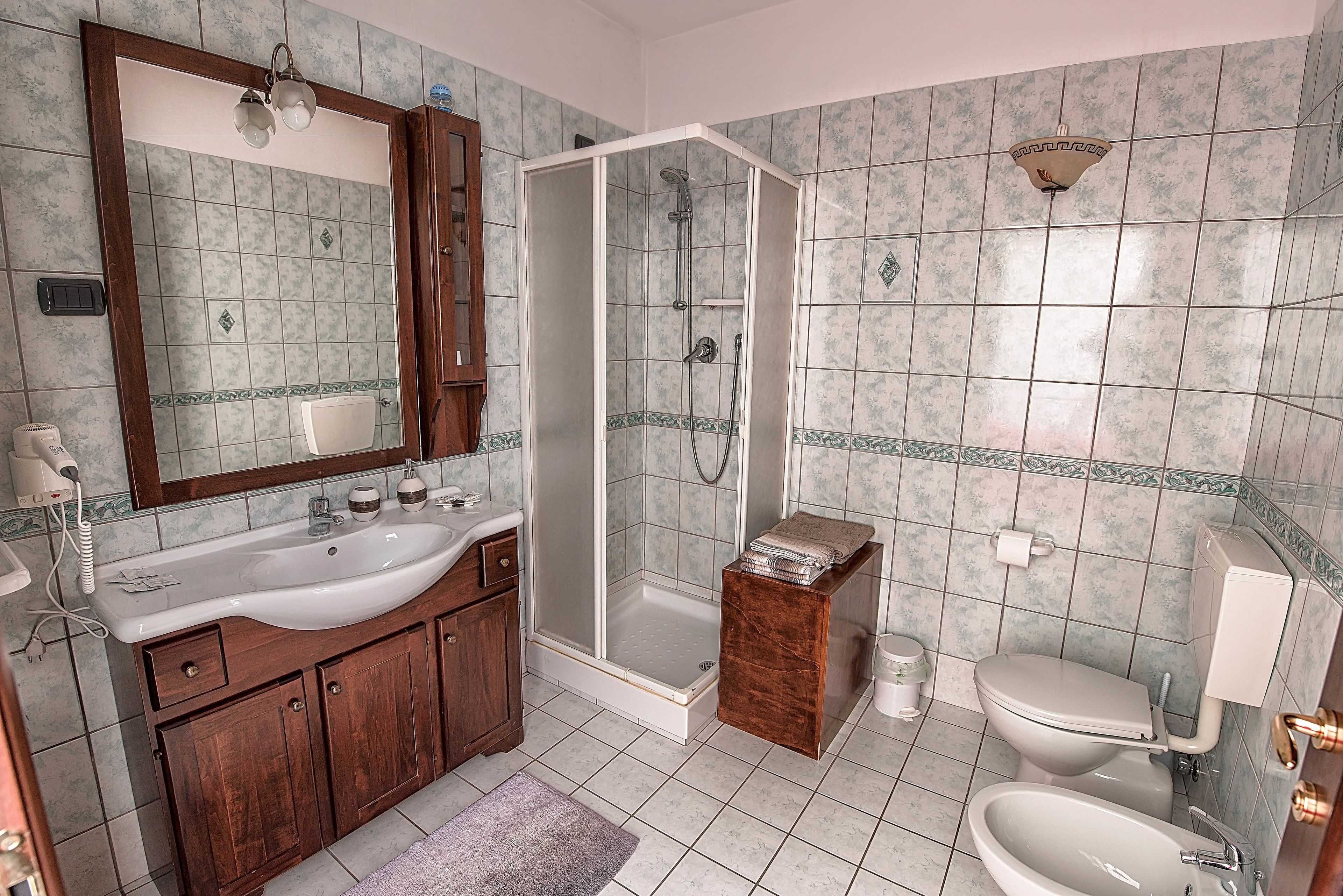 A bathroom with a wooden vanity, a sink, a toilet, a shower enclosure, and a mirror.