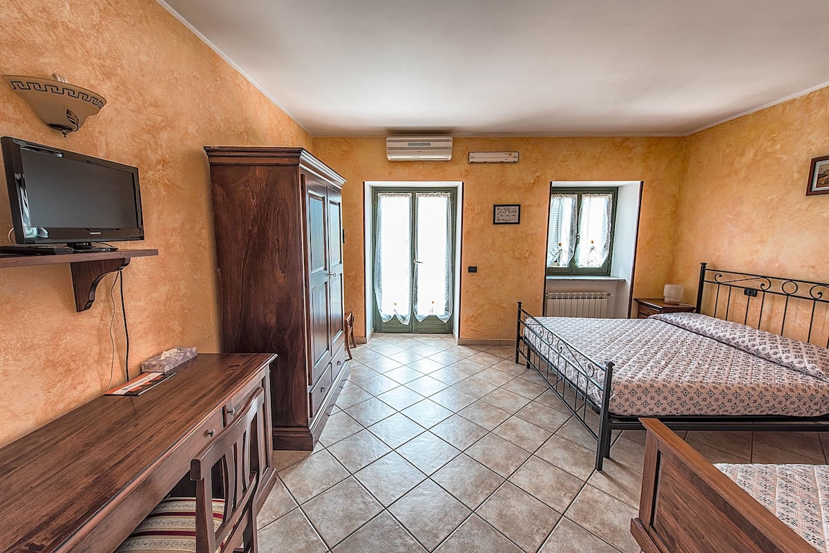 A bedroom with a bed, a TV, a wardrobe, and a door leading to a balcony.