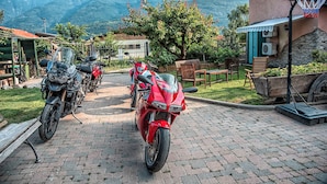 Un camino pavimentado con motocicletas estacionadas, un aro de baloncesto y una vista de montañas al fondo.