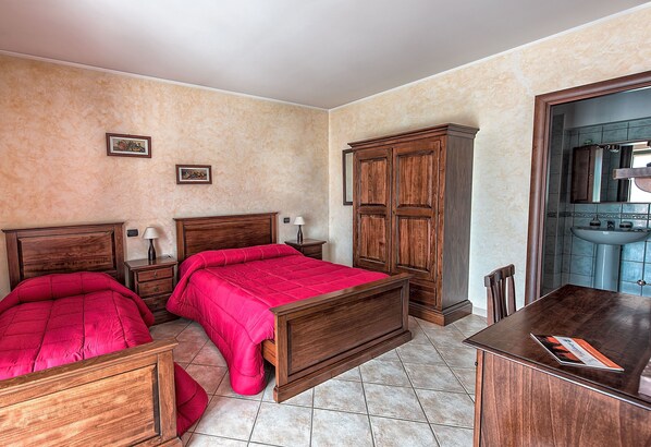 A bedroom with two wooden beds, a wooden dresser, and a bathroom visible through an open door.