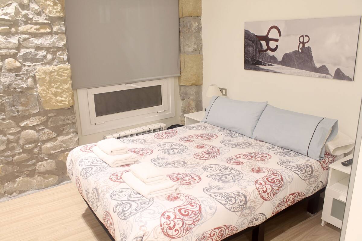 A bedroom with a bed, a window, a stone wall, and a painting on the wall.
