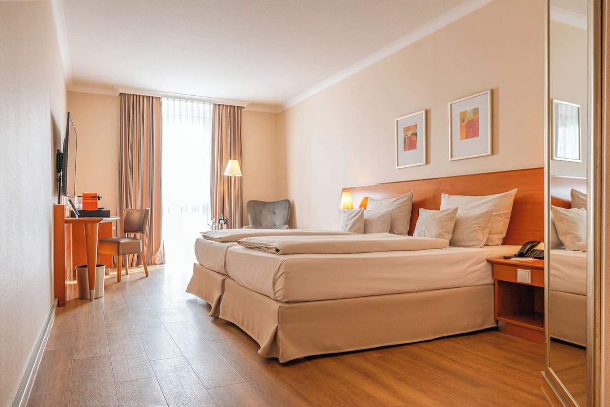 A hotel room with a large bed, a desk with a chair, a TV, and artwork on the wall.