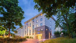 A modern hotel with a glass entrance, surrounded by greenery and a cobblestone path. - PhiLeRo Hotel Köln (Cologne)