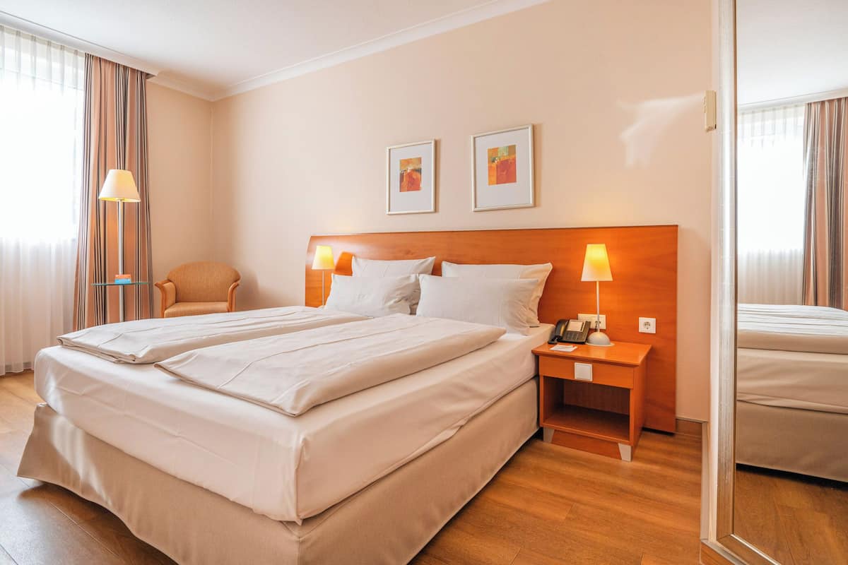 A hotel room with a large bed, two bedside tables with lamps, a chair, and artwork on the wall.