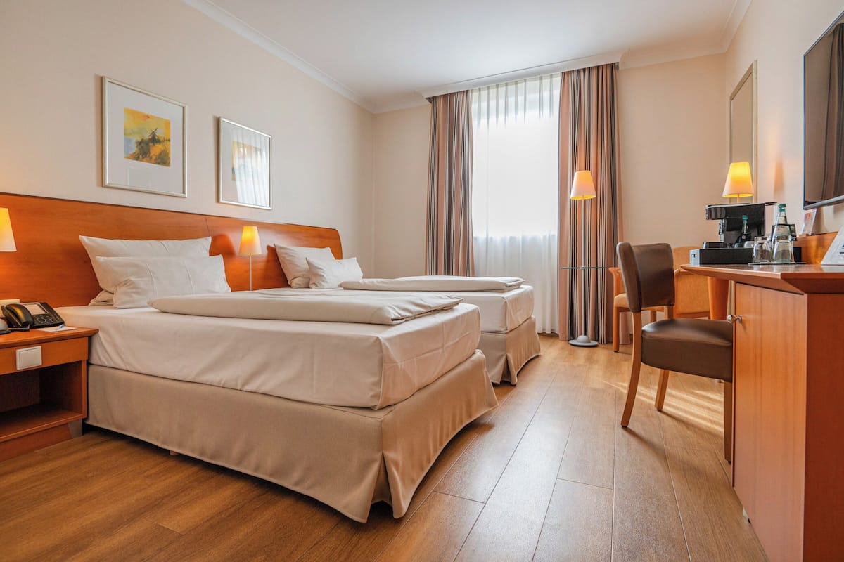 A hotel room with two beds, a desk, a chair, and a minibar.