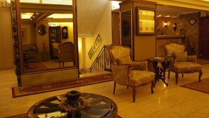 A spacious lobby with a grand staircase, elegant armchairs, a round table with a decorative centerpiece, and a large mirror reflecting the room. - Hotel Nezih Istanbul (Istanbul)