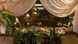A cozy room with a large window, a wooden table, and several chairs. There are potted plants and a vase with flowers on the table. - Hotel Nezih Istanbul (Istanbul)