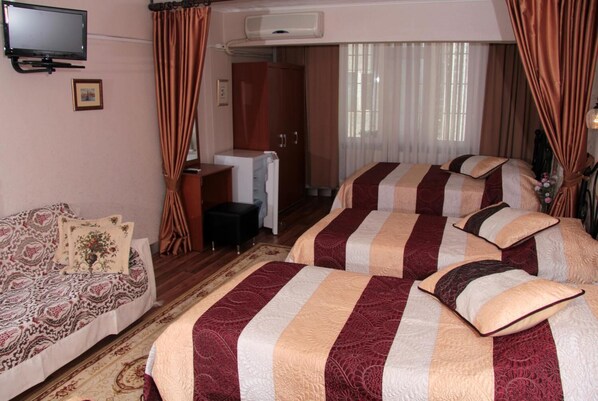 Habitación de hotel con sofá, dos camas con ropa de cama a rayas, televisor, armario y ventana con cortinas.